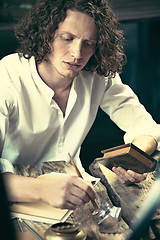 Image showing Writer at work. Handsome young writer sitting at the table and writing something in his sketchpad