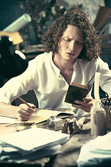 Image showing Writer at work. Handsome young writer sitting at the table and writing something in his sketchpad