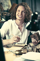 Image showing Writer at work. Handsome young writer sitting at the table and writing something in his sketchpad