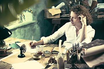 Image showing Writer at work. Handsome young writer sitting at the table and writing something in his sketchpad