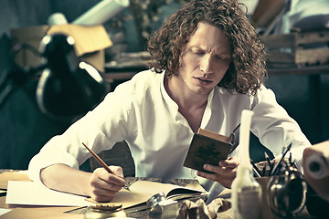 Image showing Writer at work. Handsome young writer sitting at the table and writing something in his sketchpad
