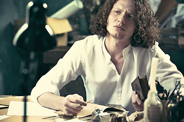 Image showing Writer at work. Handsome young writer sitting at the table and writing something in his sketchpad