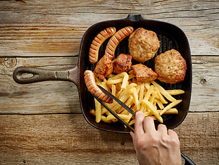 Image showing meat sausages and fried potatoes on cast iron pan