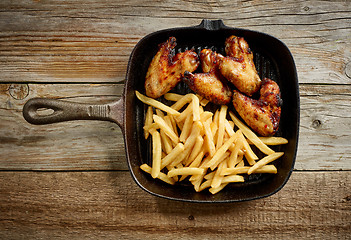 Image showing chicken wings and fried potatoes on cast iron pan