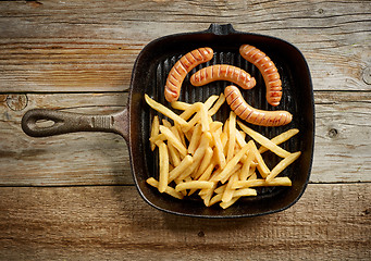 Image showing meat sausages and fried potatoes on cast iron pan