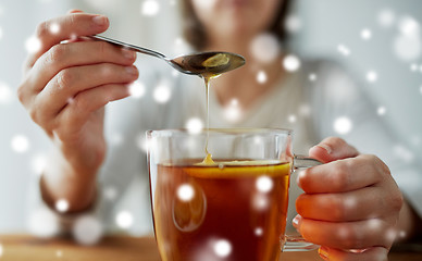 Image showing close up of woman adding honey to tea with lemon