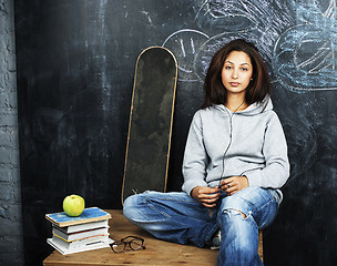 Image showing young cute teenage girl in classroom at blackboard seating on ta