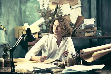 Image showing Writer at work. Handsome young writer sitting at the table and writing something in his sketchpad