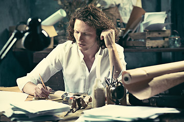 Image showing Writer at work. Handsome young writer sitting at the table and writing something in his sketchpad