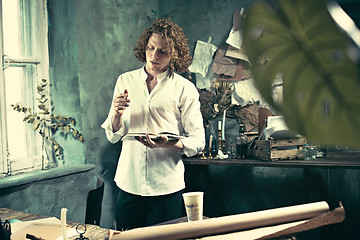 Image showing Writer at work. Handsome young writer standing near the table and making up something in his mind