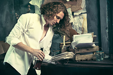 Image showing Writer at work. Handsome young writer standing near the table and making up something in his mind