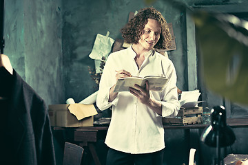 Image showing Writer at work. Handsome young writer standing near the table and making up something in his mind