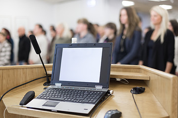 Image showing Laptop and microphone on the rostrum in lecture hall full of conference participants.