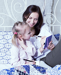 Image showing portrait of mother and daughter laying in bed reading and writing, lifestyle people concept