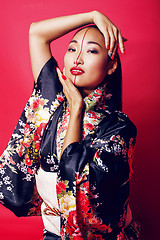 Image showing young pretty geisha on red background posing in kimono, oriental people concept