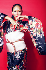 Image showing young pretty geisha on red background posing in kimono, oriental people concept