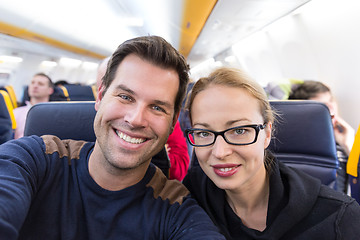 Image showing Young handsome couple taking a selfie on commercial airplane.