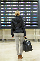 Image showing Female traveller checking a departures board at the airport terminal hall.