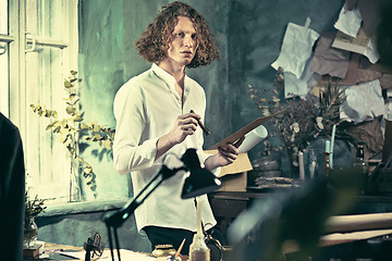 Image showing Writer at work. Handsome young writer standing near the table and making up something in his mind