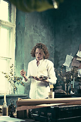 Image showing Writer at work. Handsome young writer standing near the table and making up something in his mind