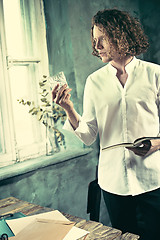 Image showing Writer at work. Handsome young writer standing near the table and making up something in his mind