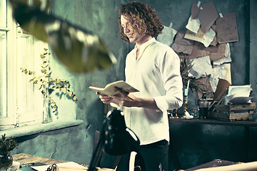 Image showing Writer at work. Handsome young writer standing near the table and making up something in his mind