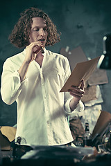 Image showing Writer at work. Handsome young writer standing near the table and making up something in his mind