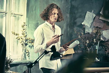 Image showing Writer at work. Handsome young writer standing near the table and making up something in his mind