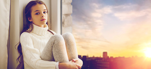 Image showing sad girl sitting on sill at home window