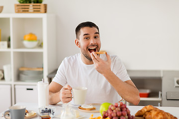 Image showing man eating toast with coffee at home kitchen