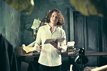 Image showing Writer at work. Handsome young writer standing near the table and making up something in his mind