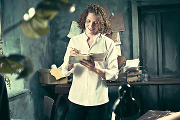 Image showing Writer at work. Handsome young writer standing near the table and making up something in his mind