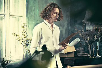 Image showing Writer at work. Handsome young writer standing near the table and making up something in his mind