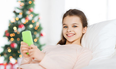 Image showing happy girl in bed with smartphone at christmas