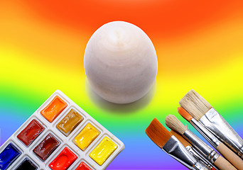 Image showing Wooden not painted egg on the background of a rainbow and a brush with paints, the concept of coloring the world with paints