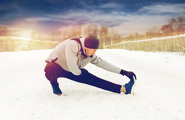 Image showing man exercising and stretching leg on winter bridge