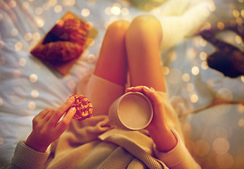 Image showing close up of woman with cocoa cup and cookie in bed