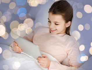 Image showing happy girl in bed with tablet pc over lights