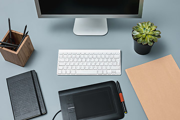 Image showing The gray desk with laptop, notepad with blank sheet, pot of flower, stylus and tablet for retouching