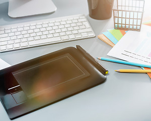 Image showing The gray desk with laptop, notepad with blank sheet, pot of flower, stylus and tablet for retouching