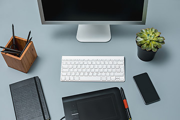 Image showing The gray desk with laptop, notepad with blank sheet, pot of flower, stylus and tablet for retouching