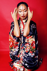 Image showing young pretty geisha on red background posing in kimono, oriental people concept 