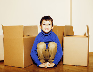 Image showing little cute boy in empty room, remoove to new house. home alone emong boxes close up kid smiling