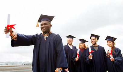 Image showing happy students in mortar boards with diplomas