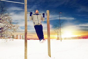 Image showing young man exercising on horizontal bar in winter