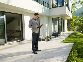 Image showing man using mobile phone in front of his luxury home villa