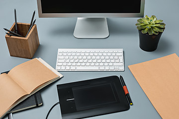 Image showing The gray desk with laptop, notepad with blank sheet, pot of flower, stylus and tablet for retouching