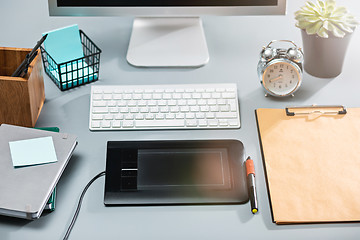 Image showing The gray desk with laptop, notepad with blank sheet, pot of flower, stylus and tablet for retouching