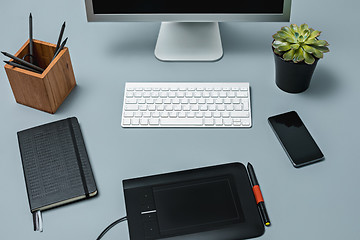 Image showing The gray desk with laptop, notepad with blank sheet, pot of flower, stylus and tablet for retouching