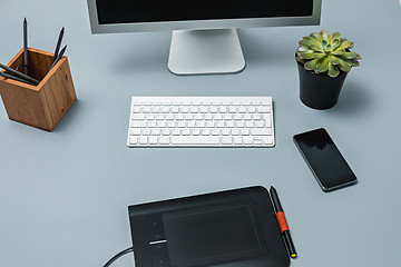 Image showing The gray desk with laptop, notepad with blank sheet, pot of flower, stylus and tablet for retouching